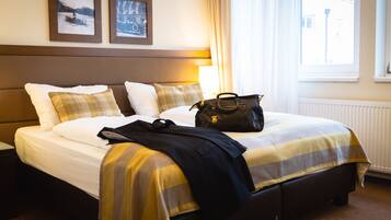 Una cama bien hecha con una colcha a rayas, un bolso negro sobre la cama y una lámpara a su lado.