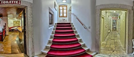 A staircase with red carpet leading to a room with a stone wall and a window.