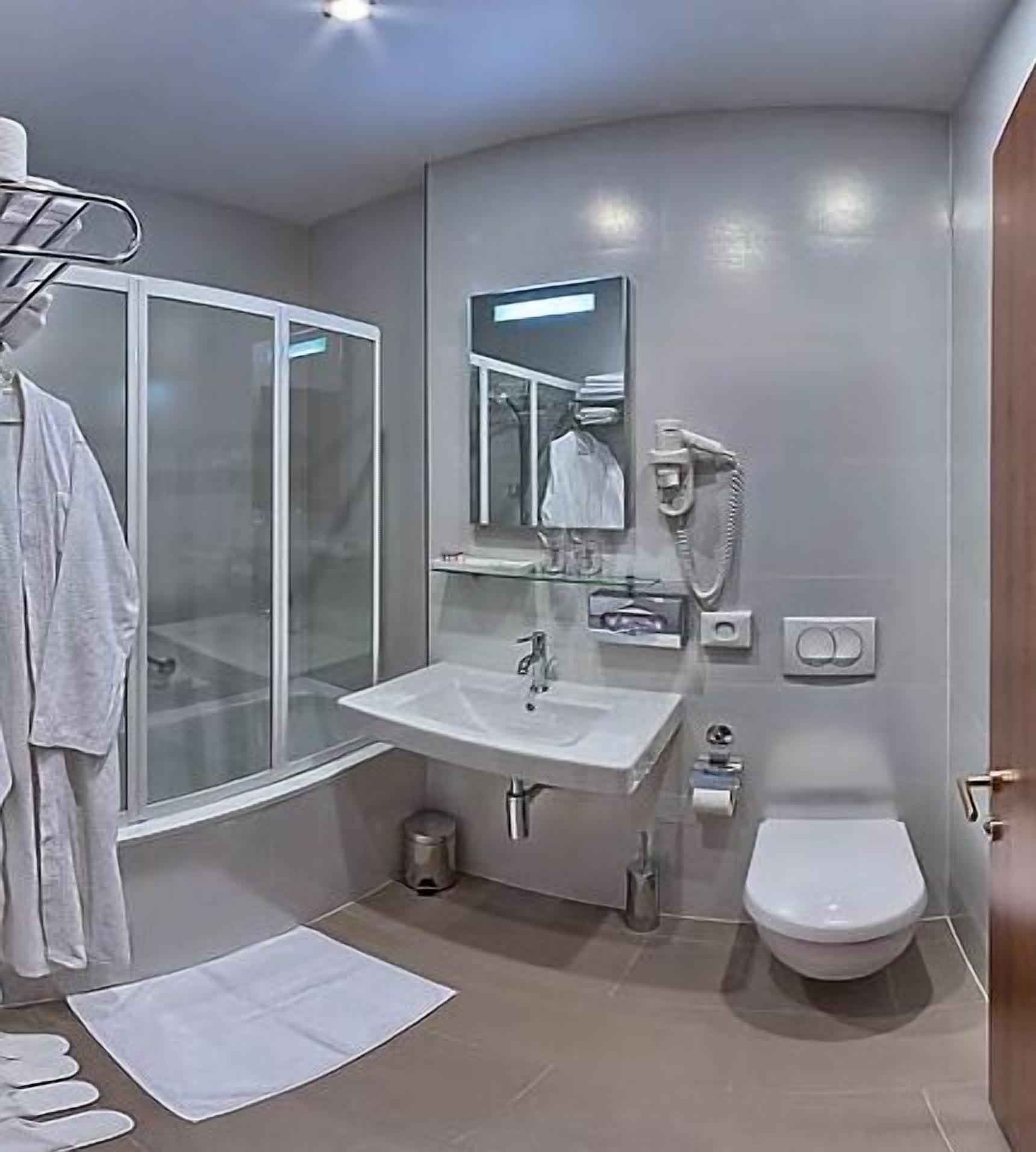 A modern bathroom with a glass-enclosed shower, a white sink, a mirror, and a toilet.