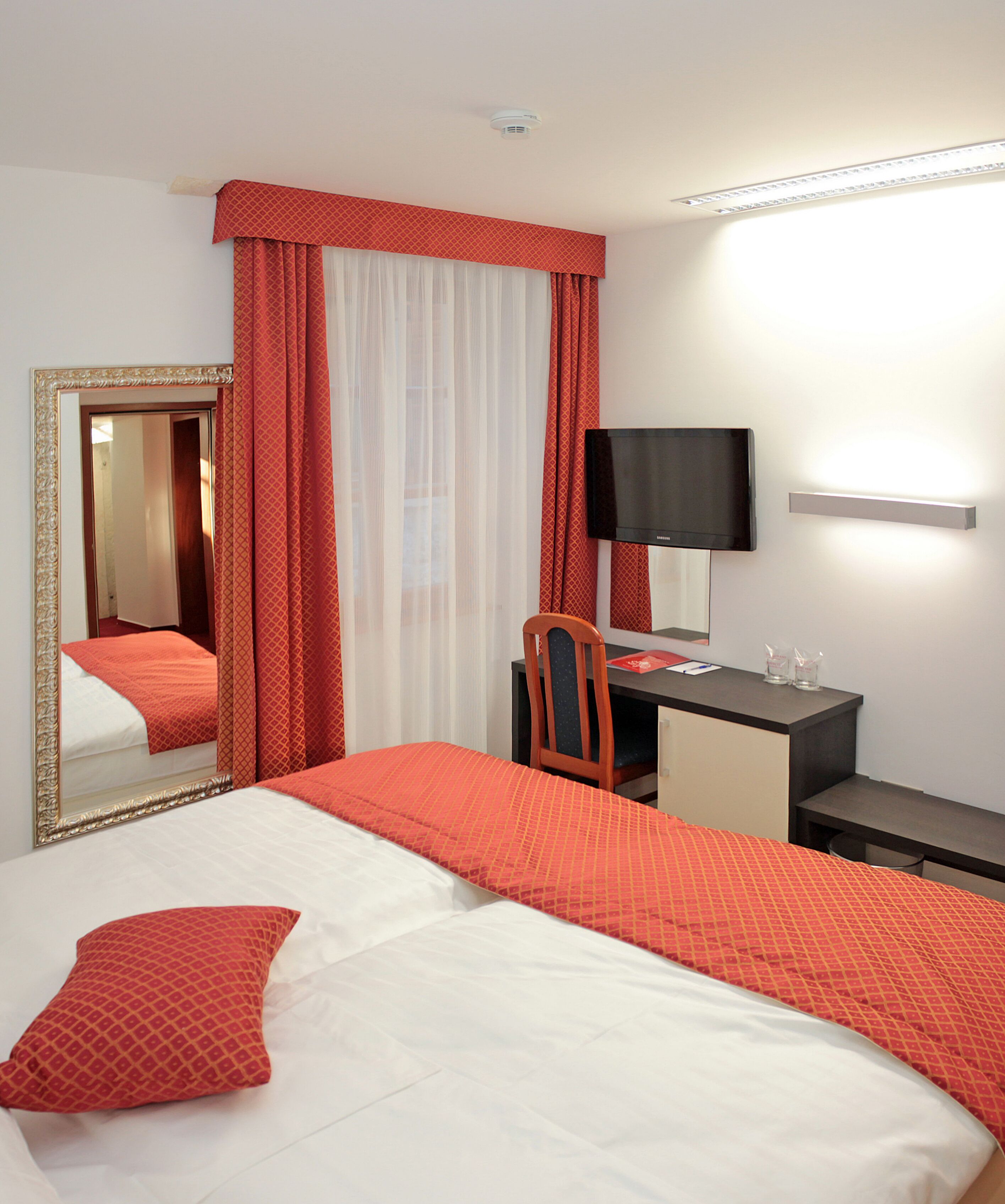 A hotel room with a bed, a desk, a chair, a TV, and a mirror.