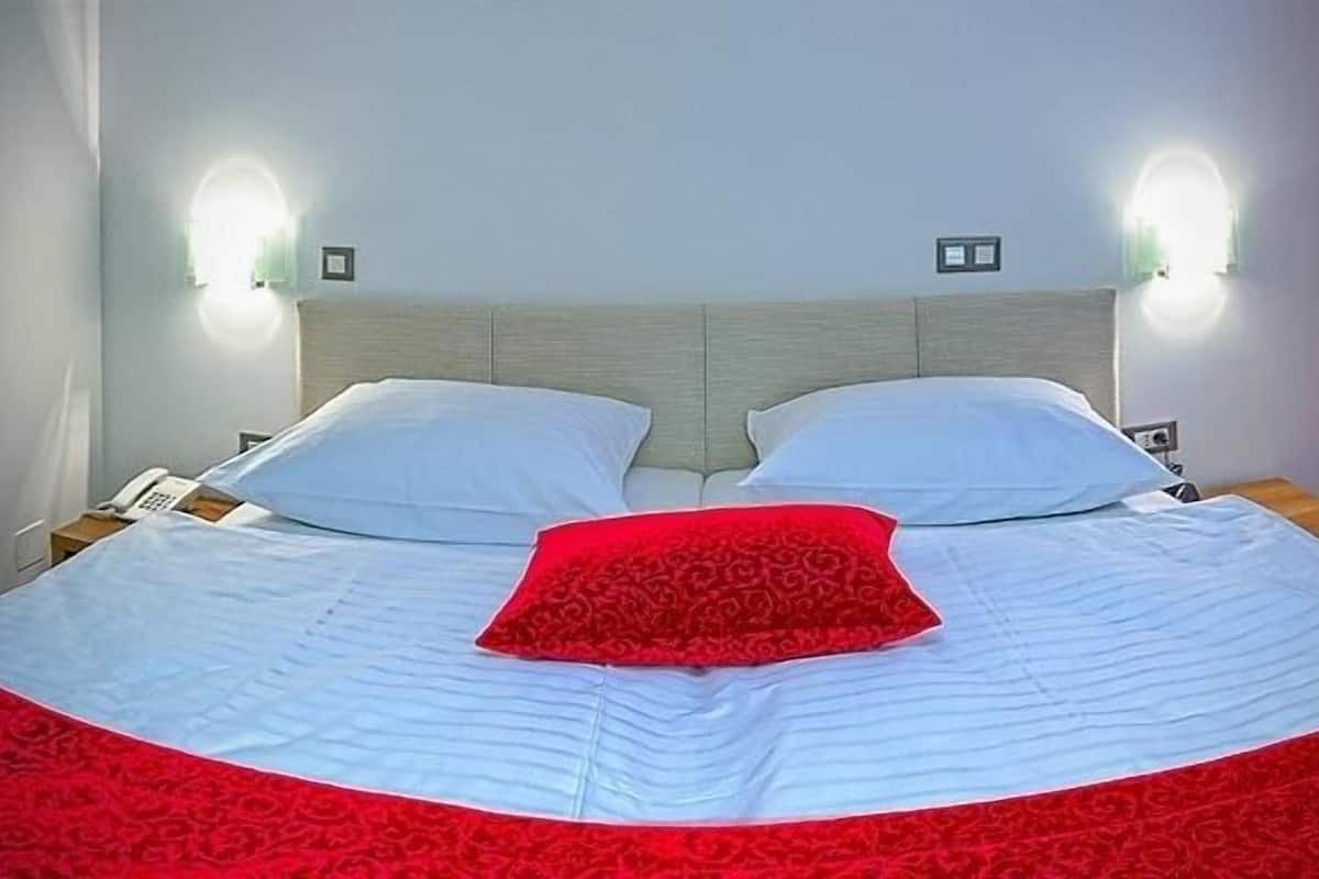 A bed with a white and red bedspread, two white pillows, and a red accent pillow. There are two bedside tables with lamps and a phone.