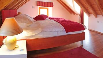 Un dormitorio con techo inclinado, una cama con ropa de cama blanca y roja, una lámpara y una alfombra roja.