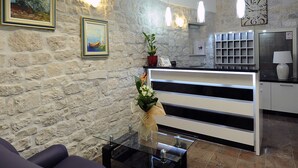 A reception area with a stone wall, a reception desk, a sofa, and a coffee table. - Hotel Monika (Trogir)