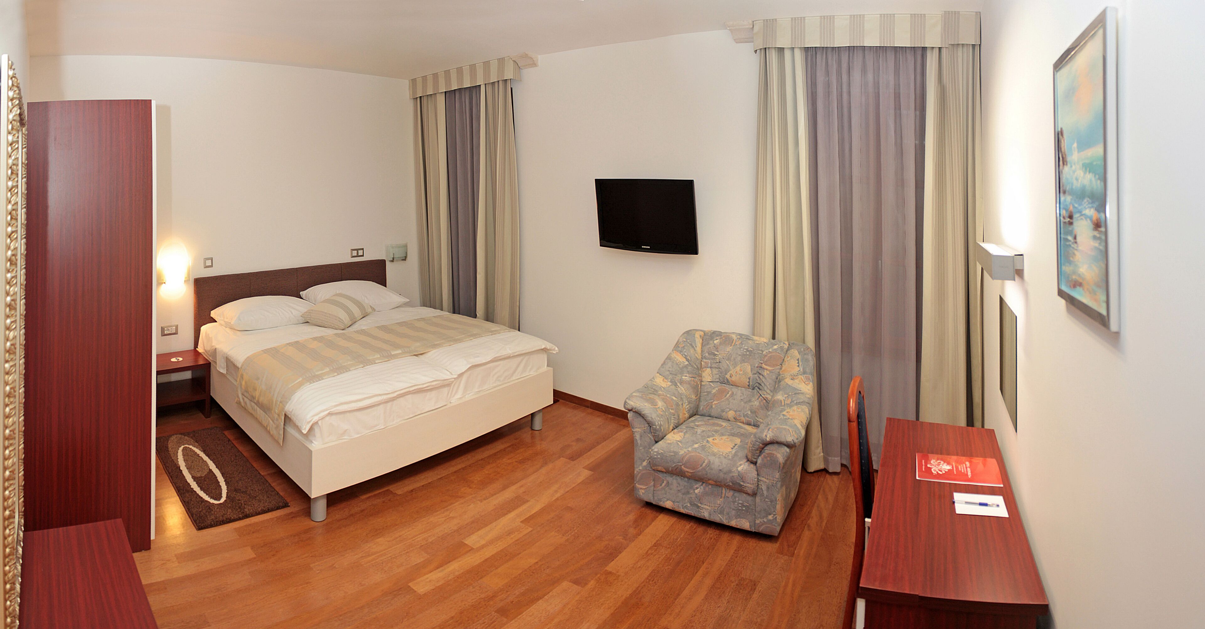 Een hotelkamer met een bed, een stoel, een bureau, een televisie en gordijnen.