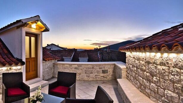 A rooftop terrace with stone walls, red-tiled roofs, and wicker furniture. - Hotel Monika (Trogir)