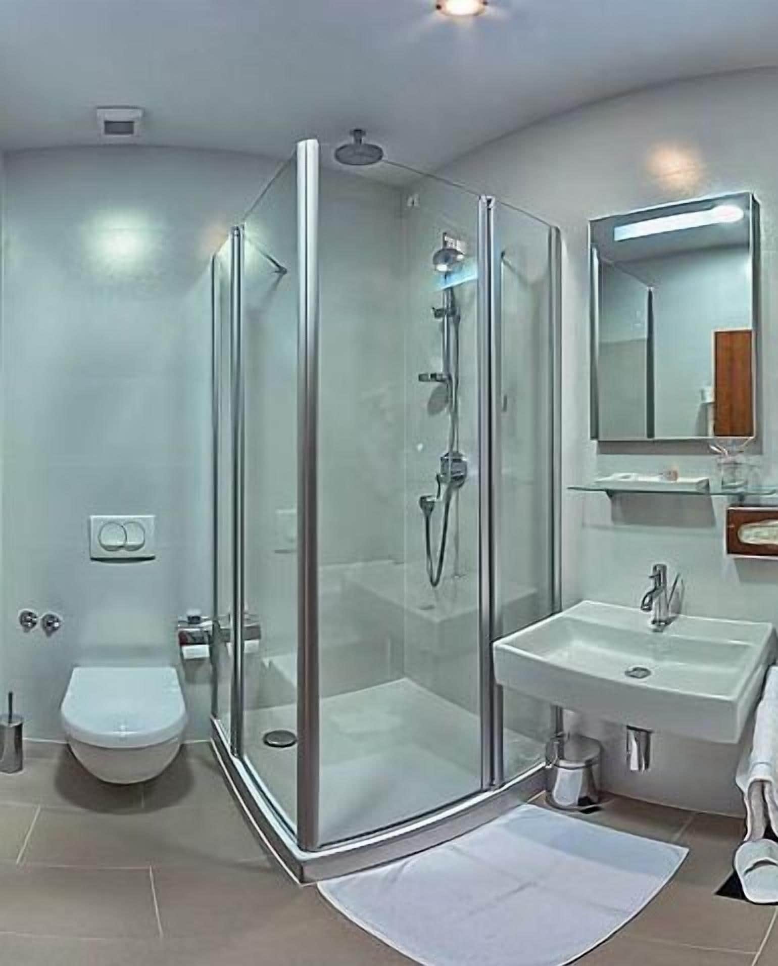 Un baño moderno con ducha de mampara de vidrio, un lavamanos blanco y un inodoro.