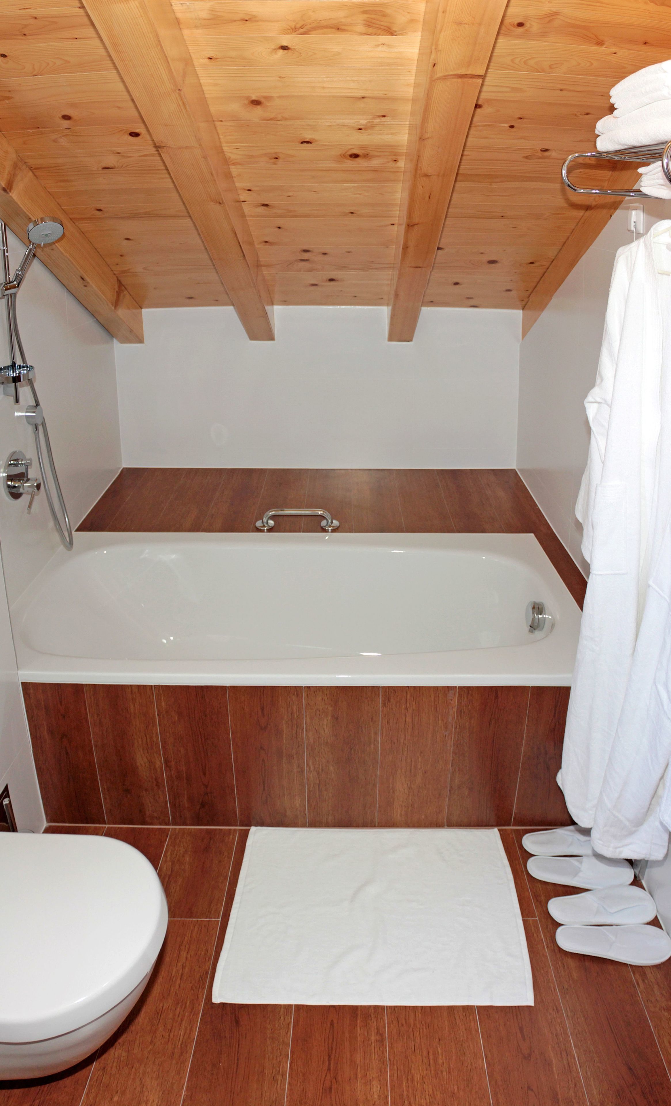 A modern bathroom with a wooden ceiling, a bathtub, a toilet, and a shower.