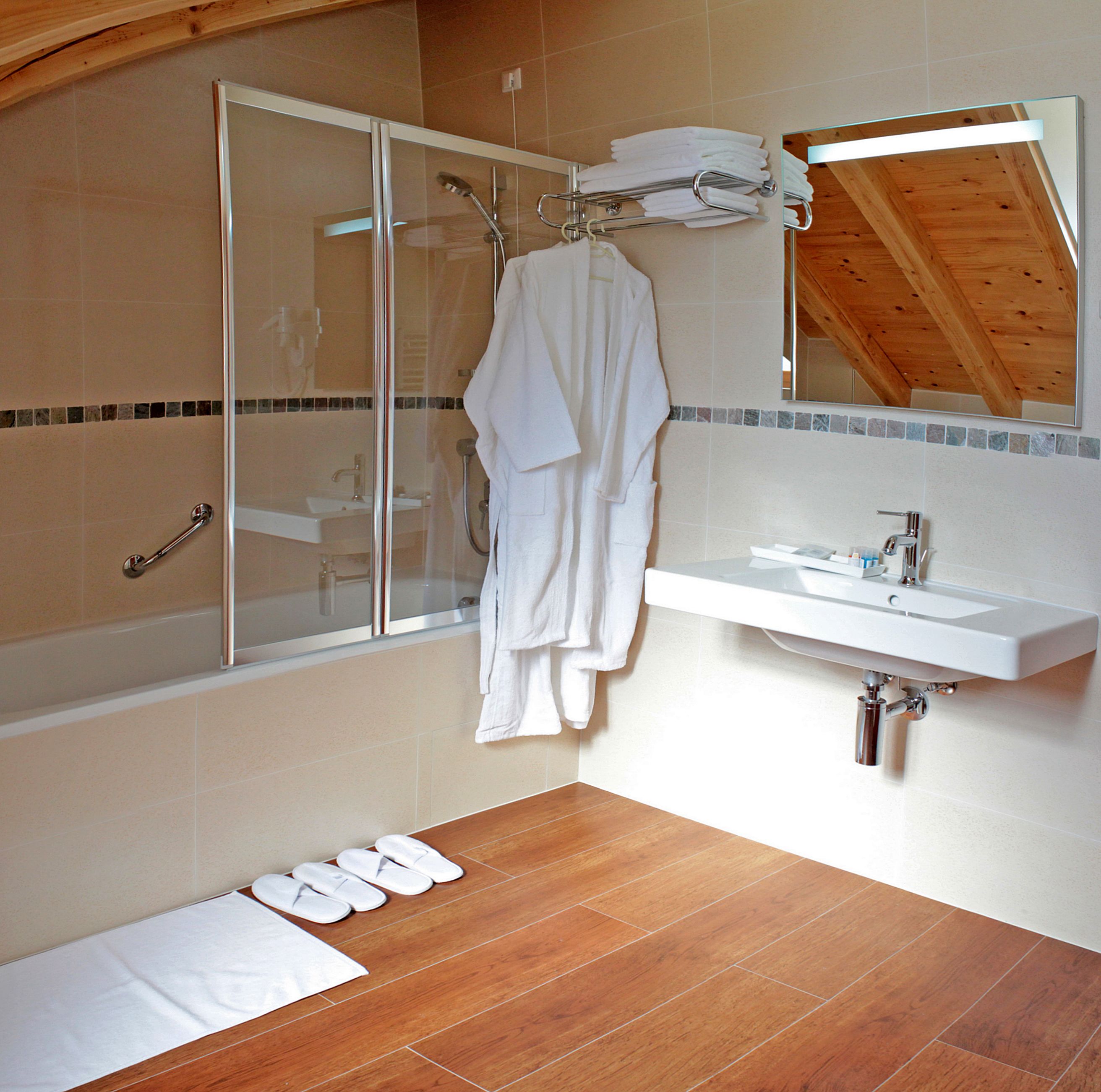 Un baño moderno con cabina de ducha de vidrio, techo de madera, lavamanos blanco y suelo de baldosas.