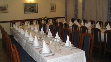 Una larga mesa de comedor cubierta con manteles blancos, copas y servilletas dobladas, rodeada de sillas de madera.