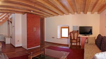A spacious living area with a wooden ceiling, a television, a sofa, and a staircase leading to another room.