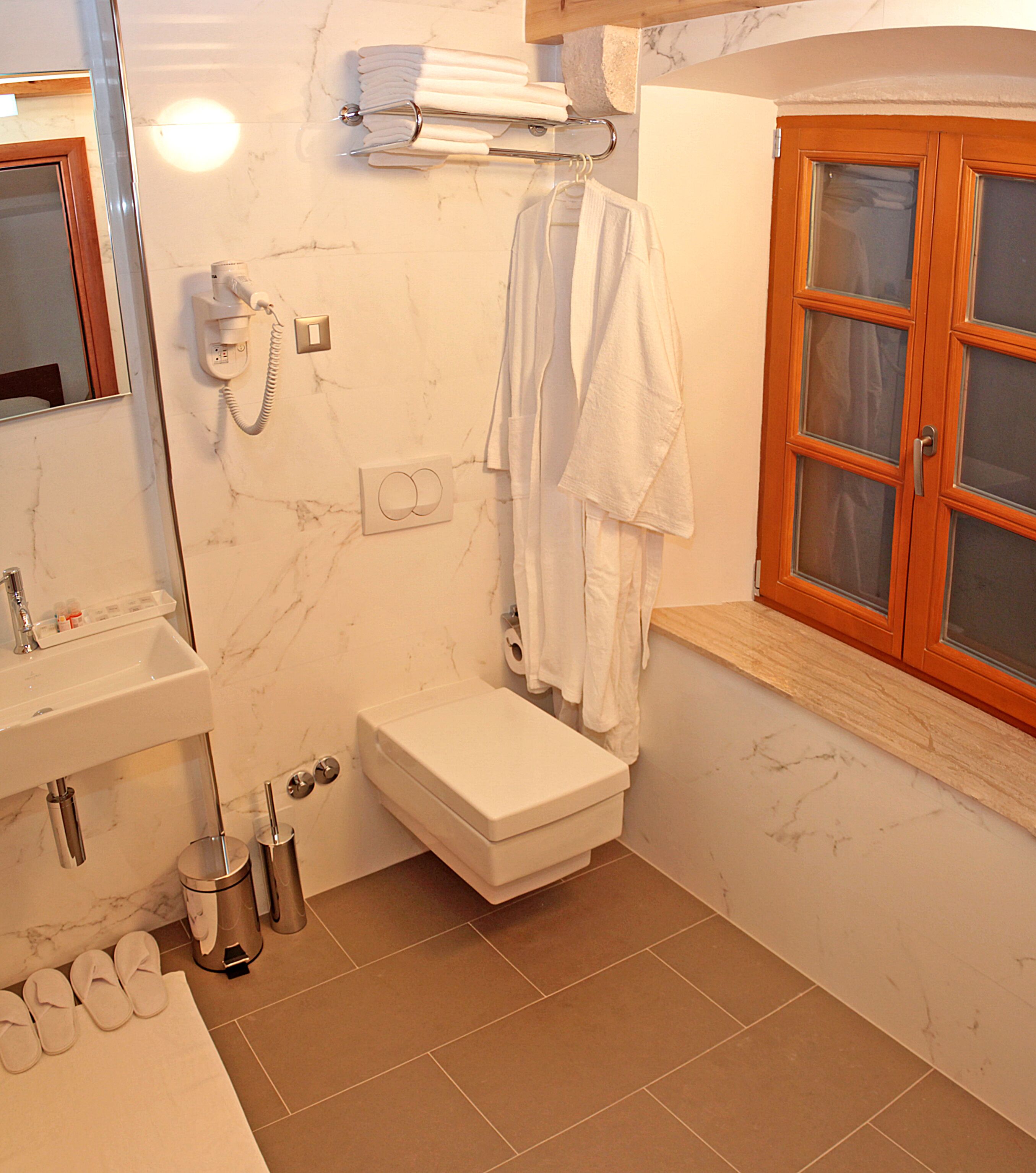 Ein Badezimmer mit Toilette, Waschbecken und einem Fenster mit Holzrahmen.