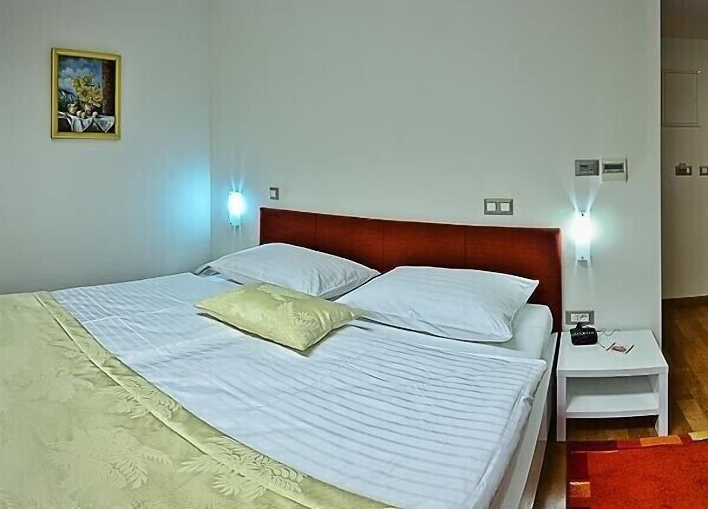 A neatly made bed with white linens and a beige pillow, a wooden headboard, and two bedside tables with lamps.