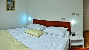 A neatly made bed with white linens and a beige pillow, a wooden headboard, and two bedside tables with lamps.