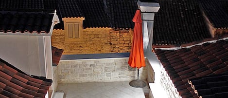 Une terrasse avec deux chaises et une table, un parasol rouge, et une vue sur une ville où l’on aperçoit, au loin, le clocher d’une église.