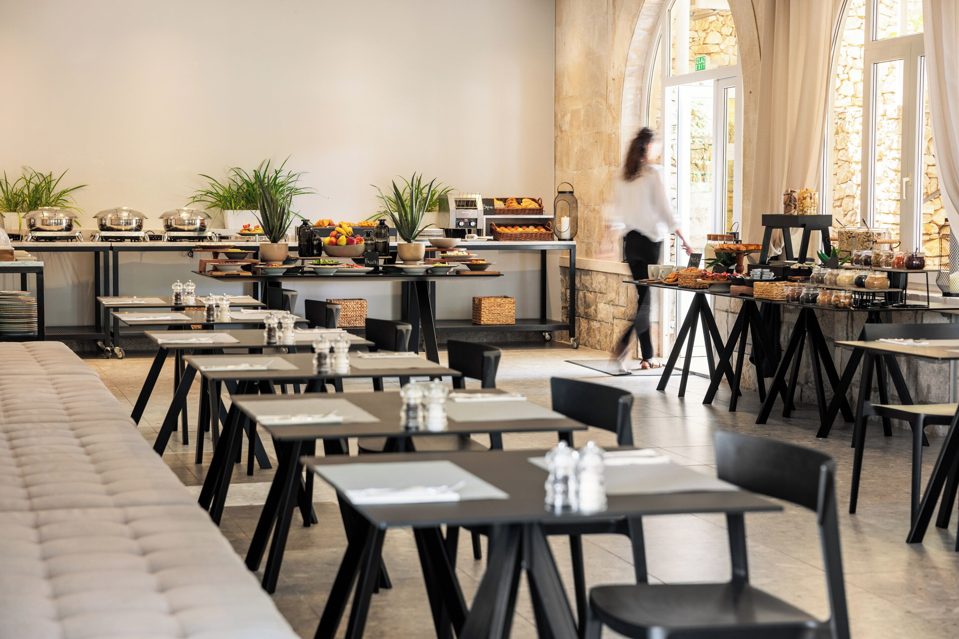 Un grand espace dédié à la salle à manger, avec plusieurs tables et chaises, un buffet proposant divers plats, et une personne qui se déplace dans cet espace.