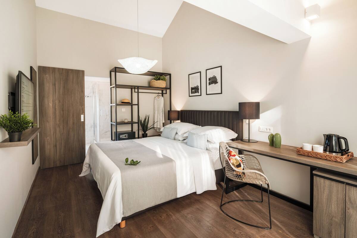 Een moderne hotelkamer met een bed, bureau, stoel en een klein kitchenette.