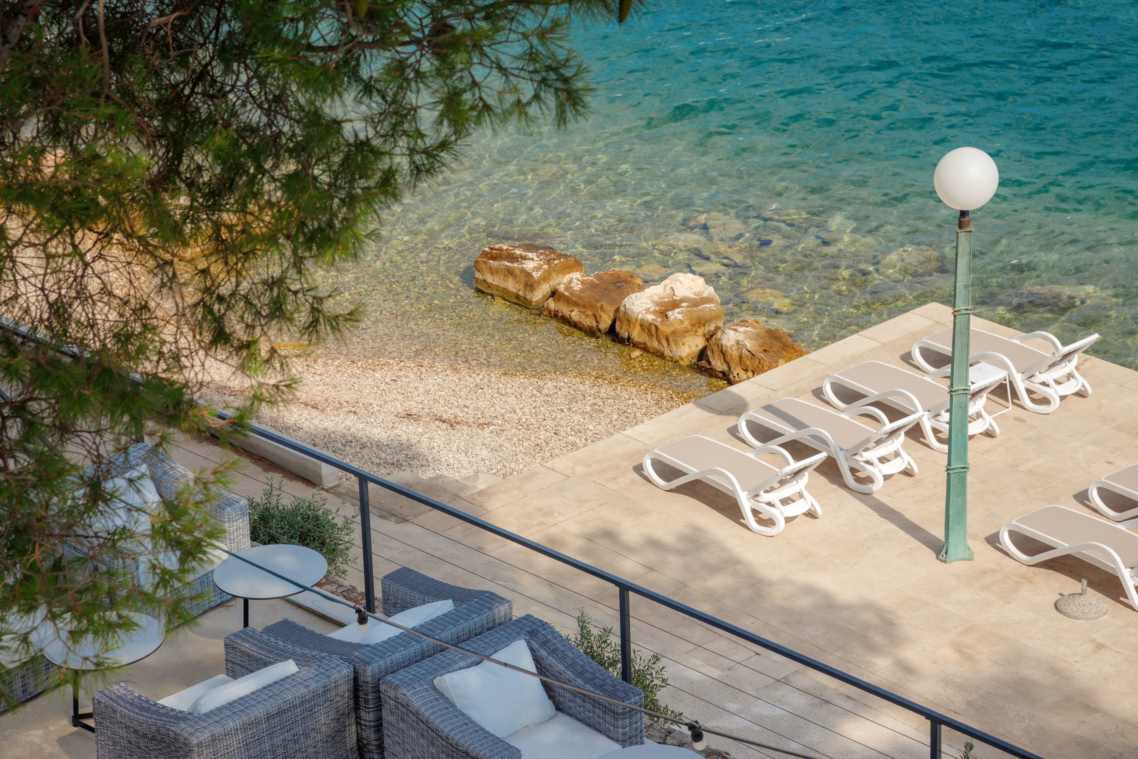 A beachside patio with wicker furniture, white lounge chairs, and a clear view of the sea.