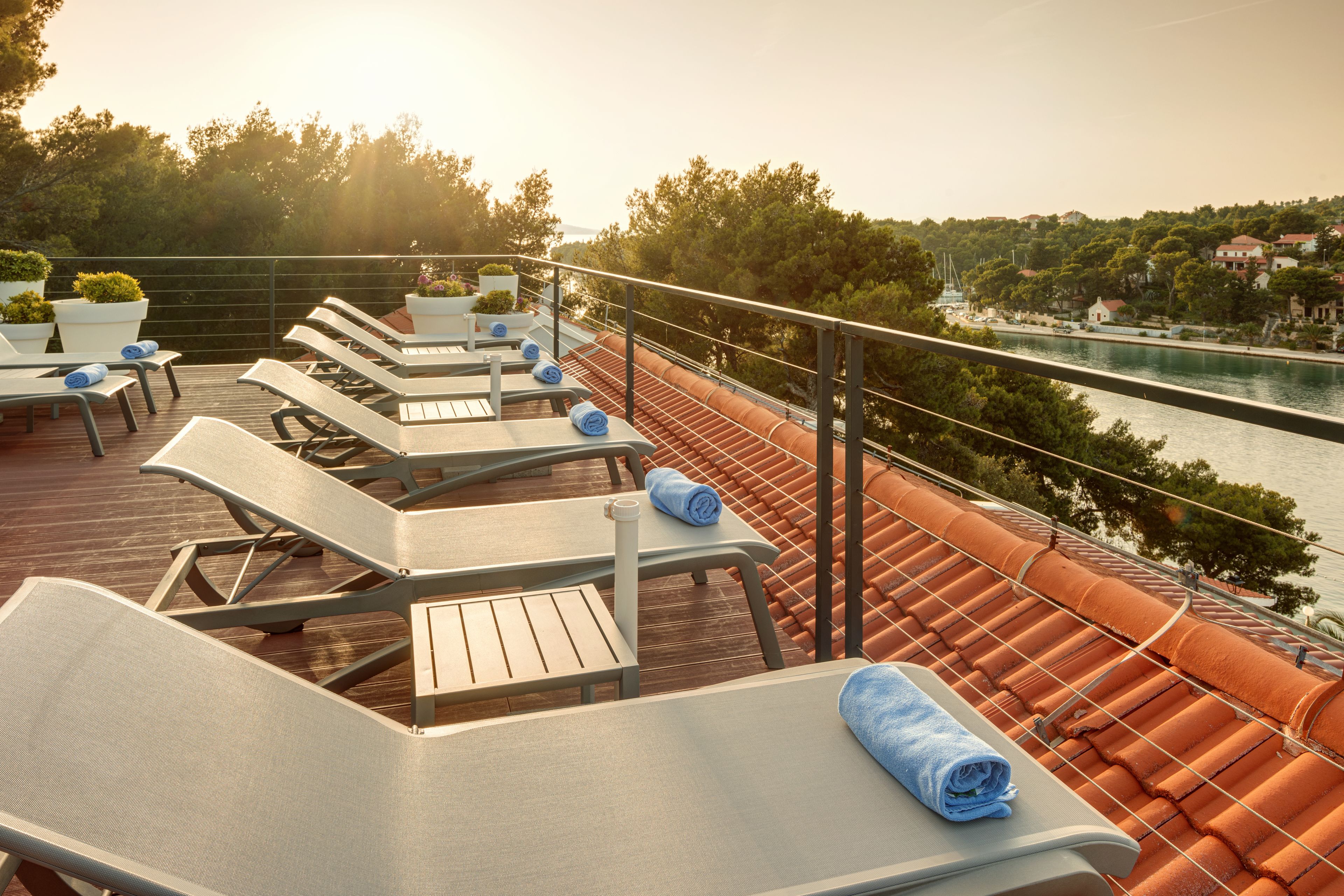 A deck with sun loungers and potted plants, overlooking a river and a town.