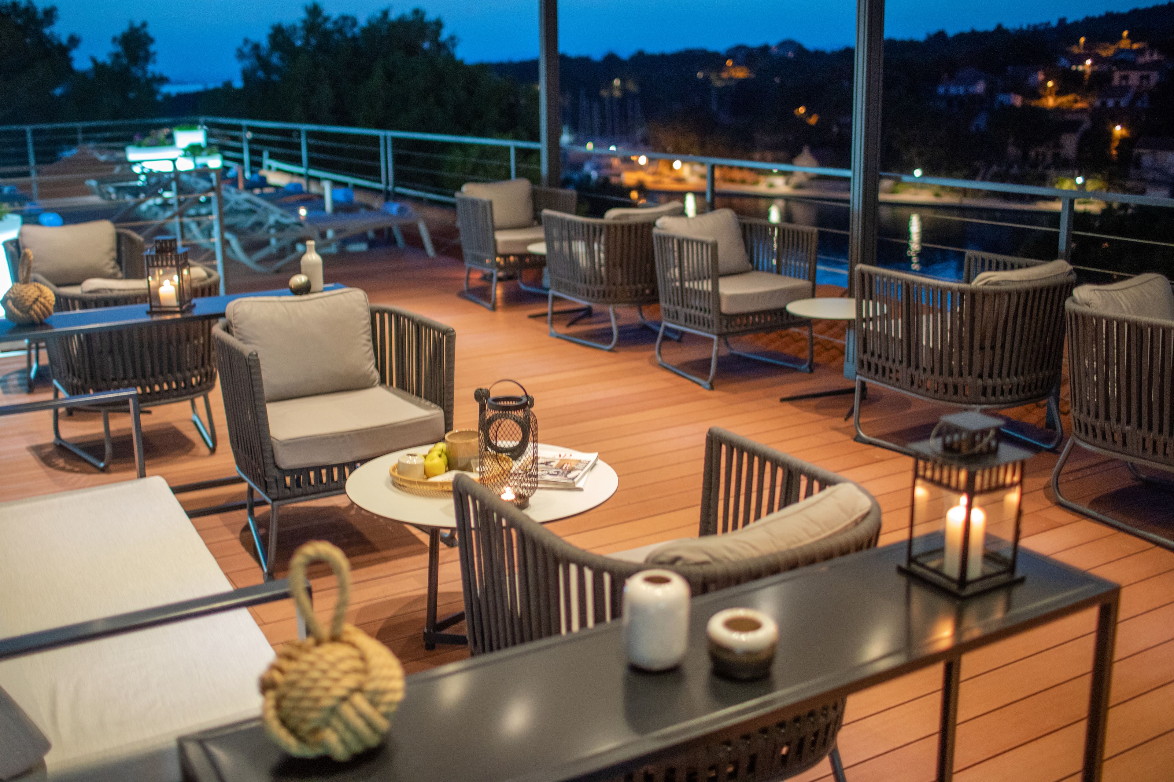En tagterrasse med fletmøbler, stearinlys og udsigt over byen i skumringen.
