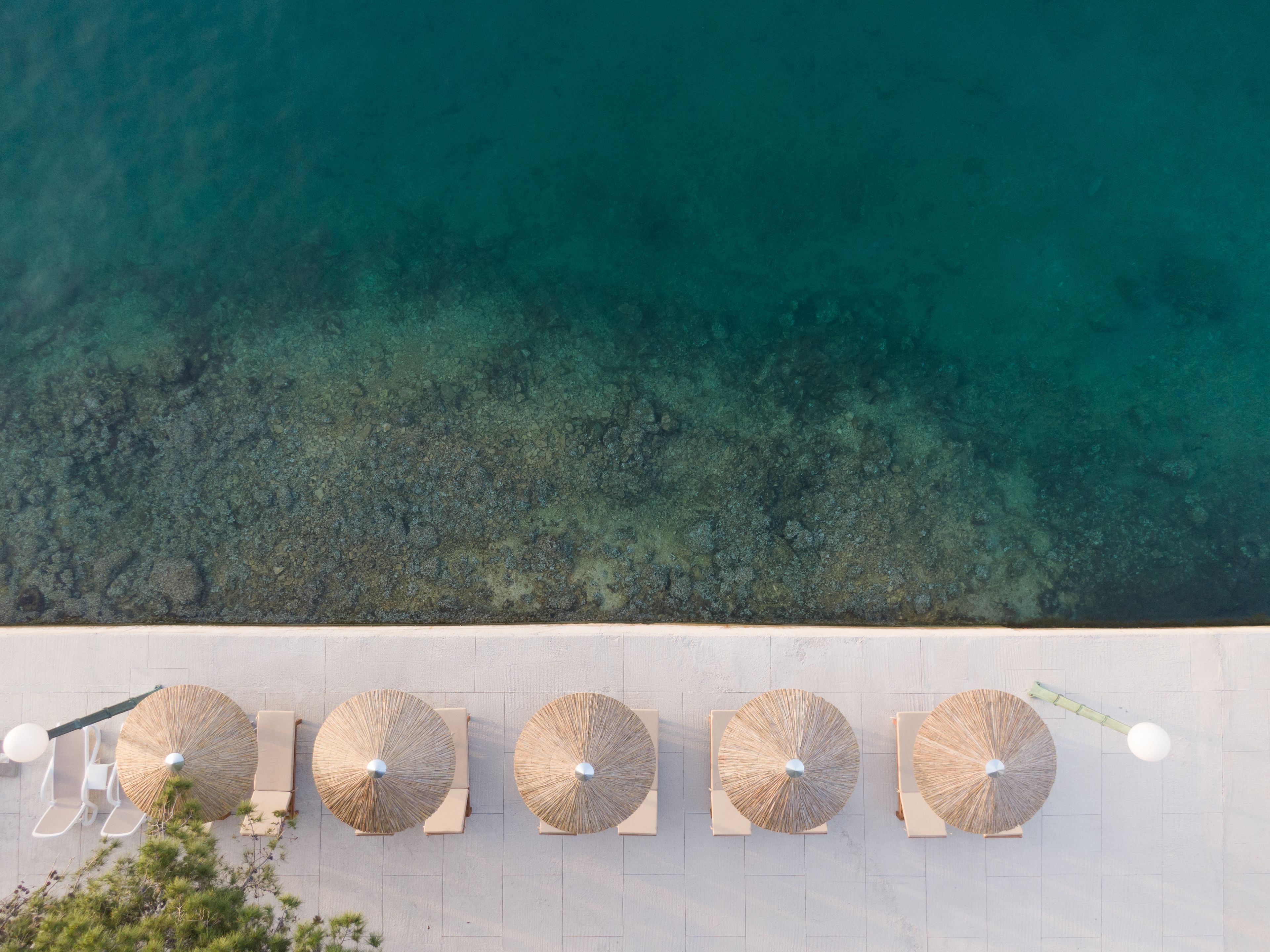 An aerial view of a beachside resort with five thatched umbrellas and lounge chairs aligned along the shoreline.