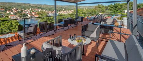 Eine Terrasse mit Sitzgelegenheiten im Freien, ein Tisch mit Getränken und Snacks und Blick auf einen See und eine Stadt.