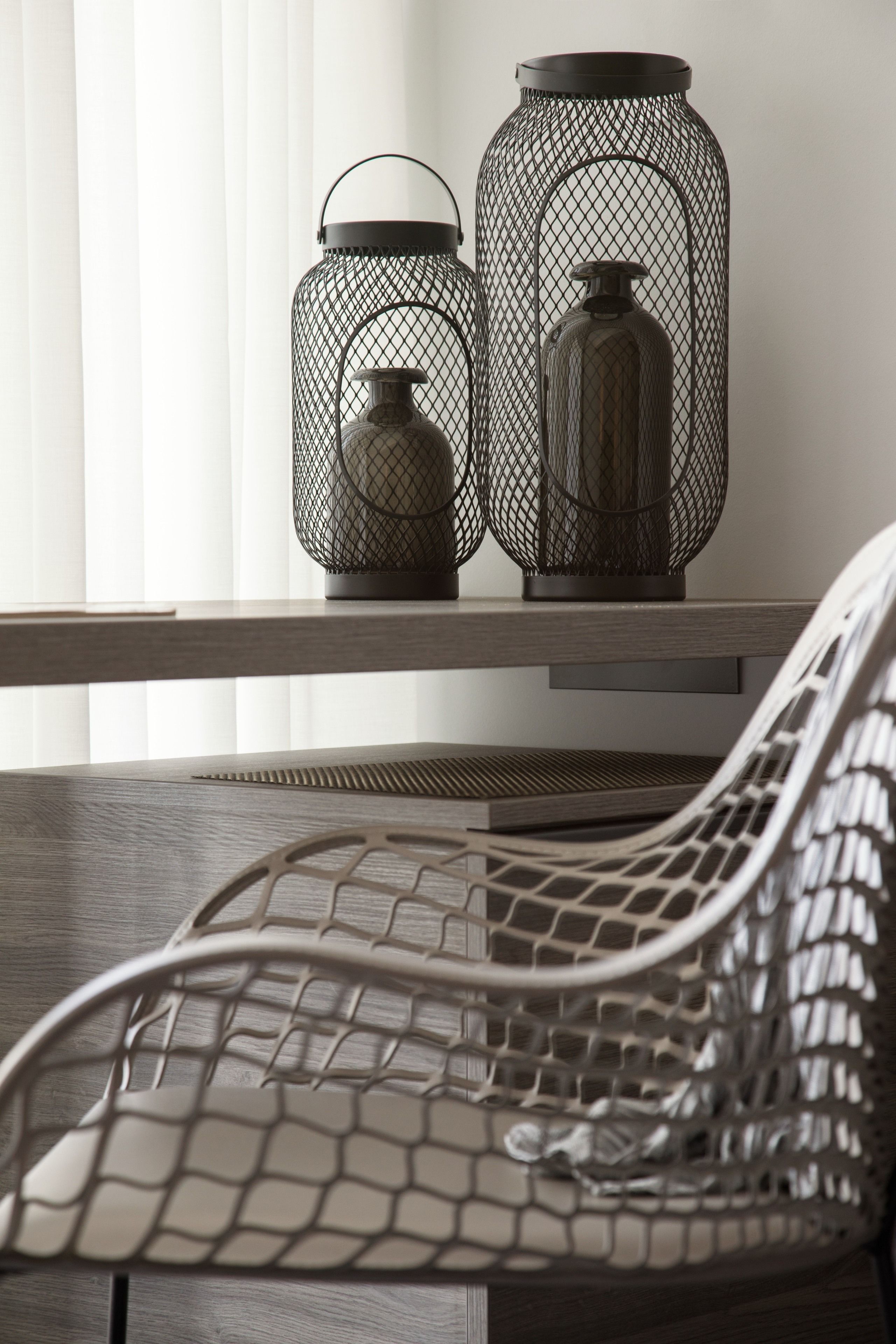 Un interior moderno con una silla y dos jarrones de malla metálica sobre un estante de madera.