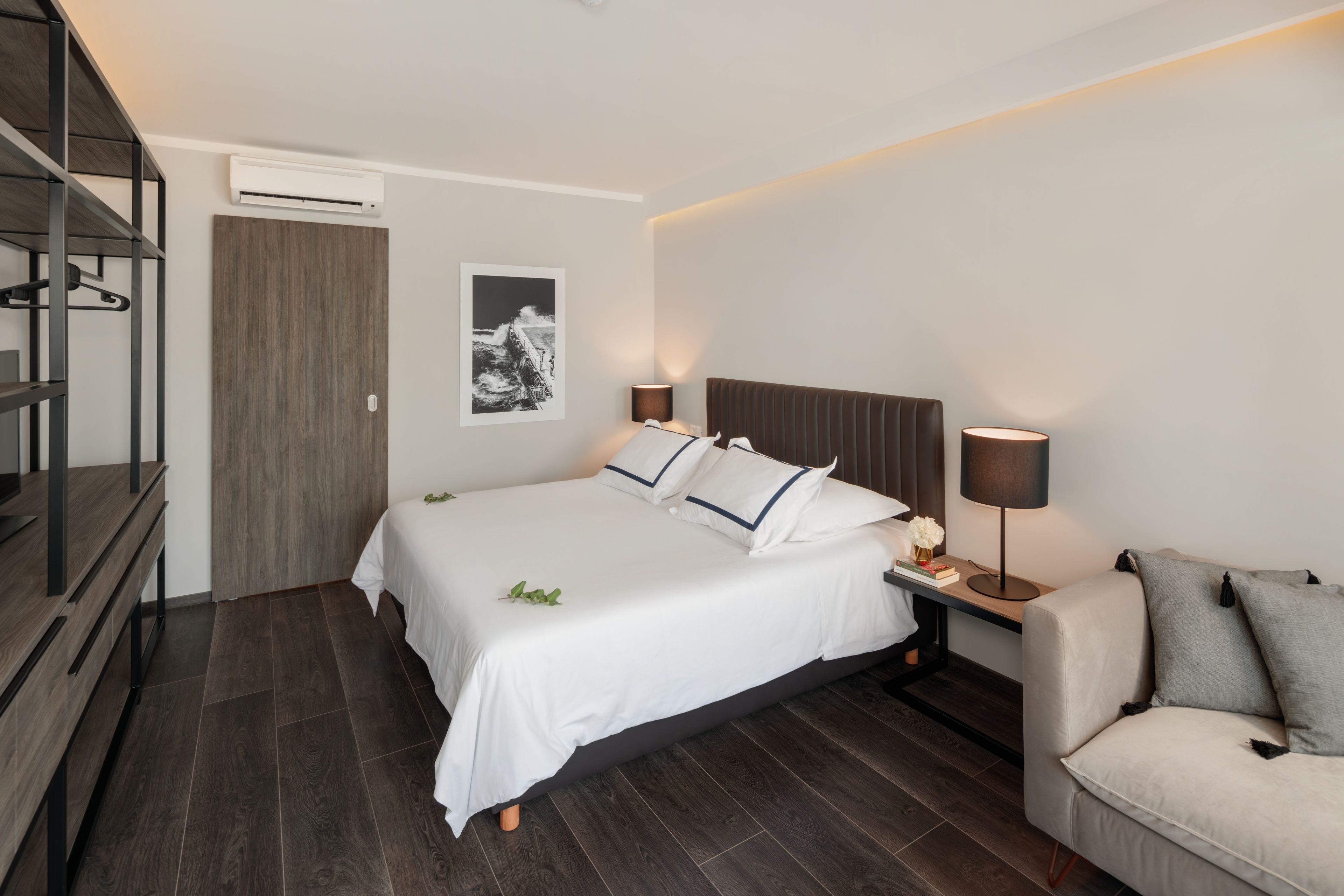 Une chambre d’hôtel moderne équipée d’un grand lit, de tables de chevet, d’un canapé, d’une armoire et d’un appareil de climatisation.
