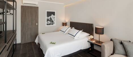 Une chambre d’hôtel moderne équipée d’un grand lit, de tables de chevet, d’un canapé, d’une armoire et d’un appareil de climatisation.