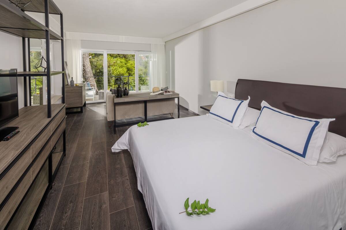 Een moderne hotelkamer met een groot bed, een bureau, een televisie en uitzicht op groen.