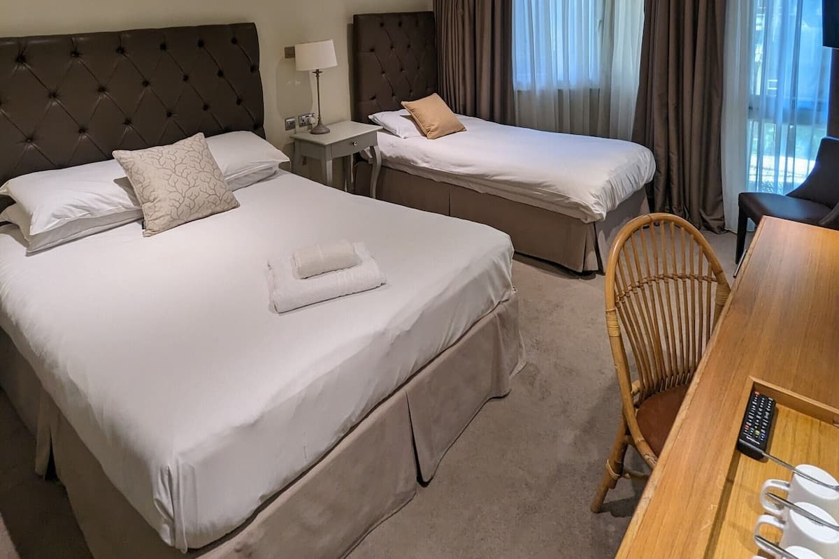 Quarto de hotel com duas camas, uma mesa com cadeira e vista para o exterior através de amplas janelas.