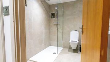 A modern bathroom with a glass-enclosed shower, a toilet, and a trash bin.