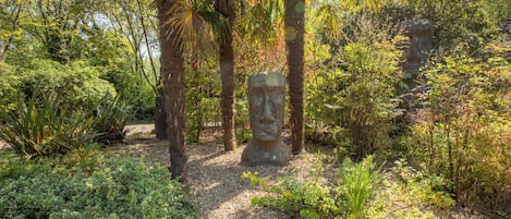 A garden with a stone statue, surrounded by various plants and trees.