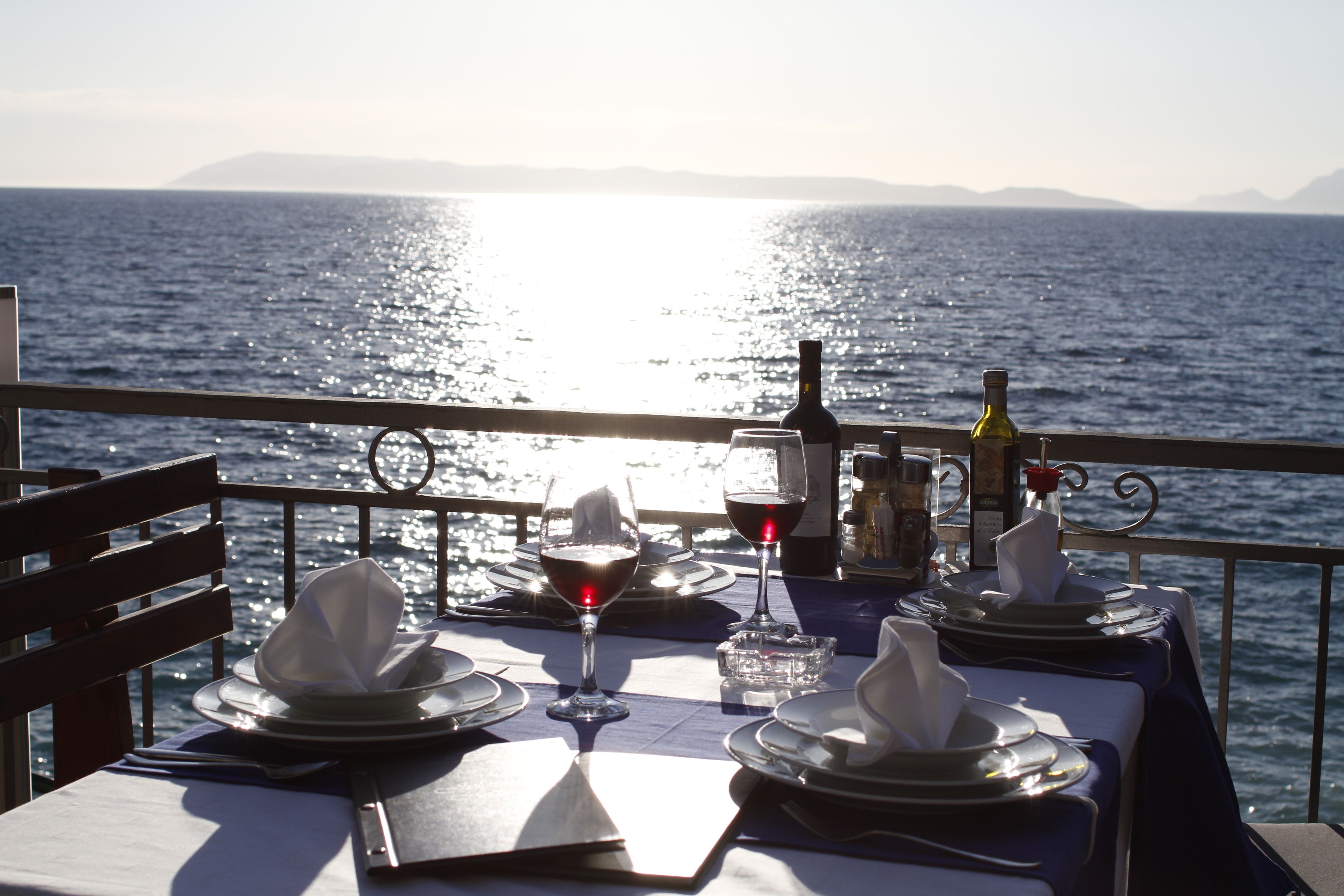 Une table dressée pour deux personnes, avec des verres à vin, une bouteille et une bougie, donnant sur une étendue d’eau.