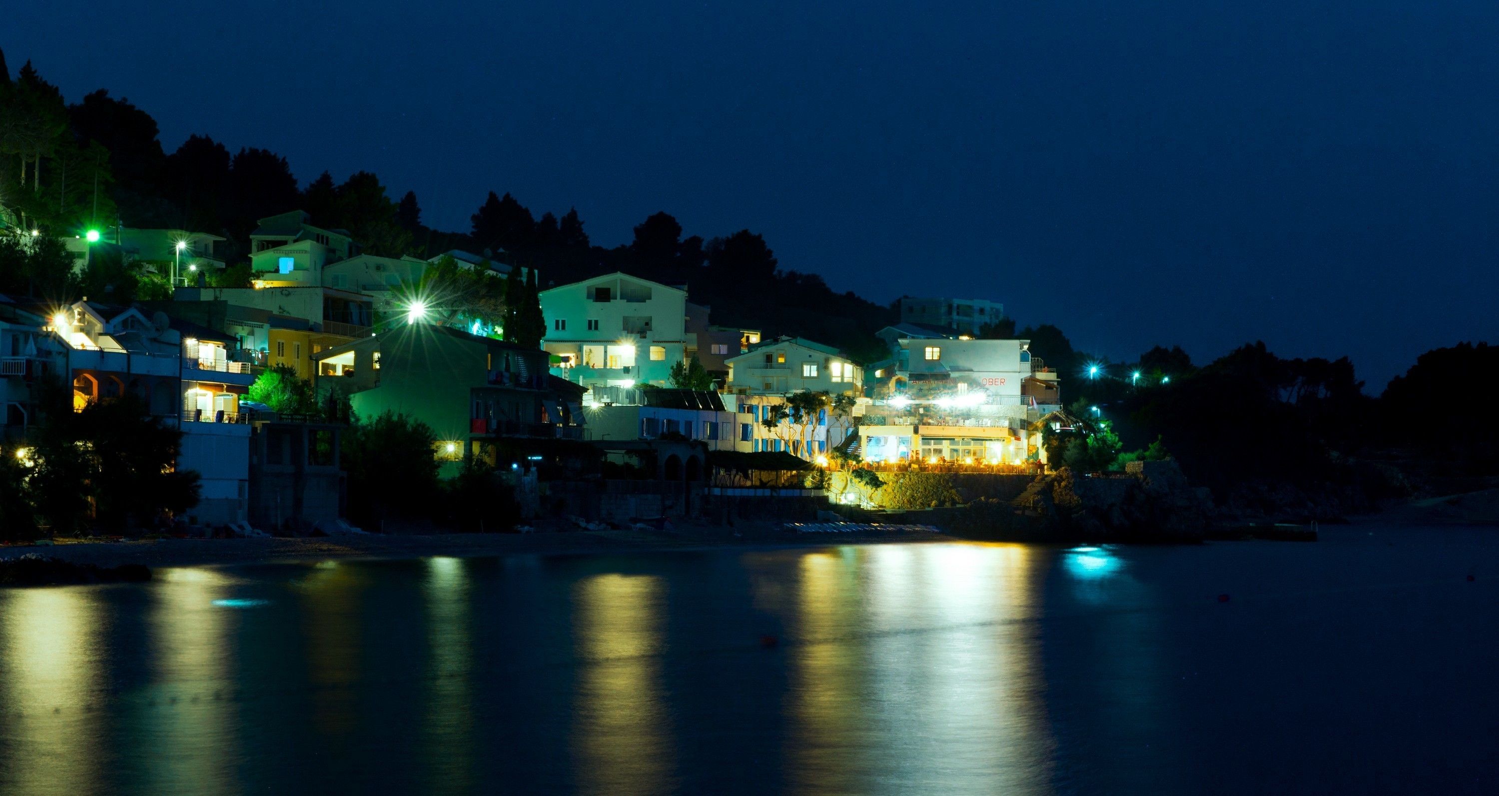 A coastal town at night with illuminated buildings reflecting on the water.
