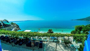 A seaside view with a clear sky, a beach with umbrellas, and a building with a green roof. - Beach Hotel Plaza (Podgora)