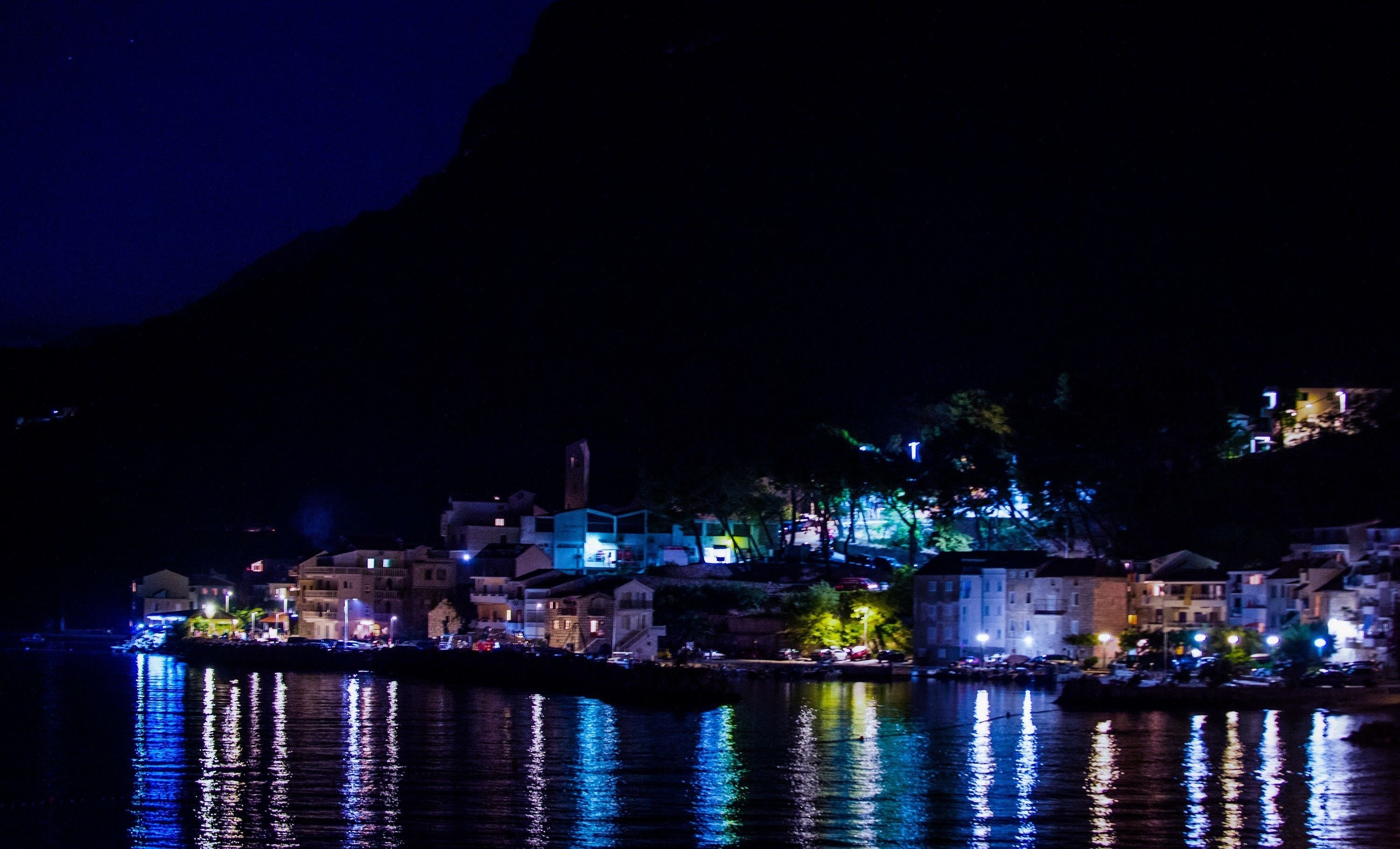 A nighttime coastal town with buildings reflected in calm waters.