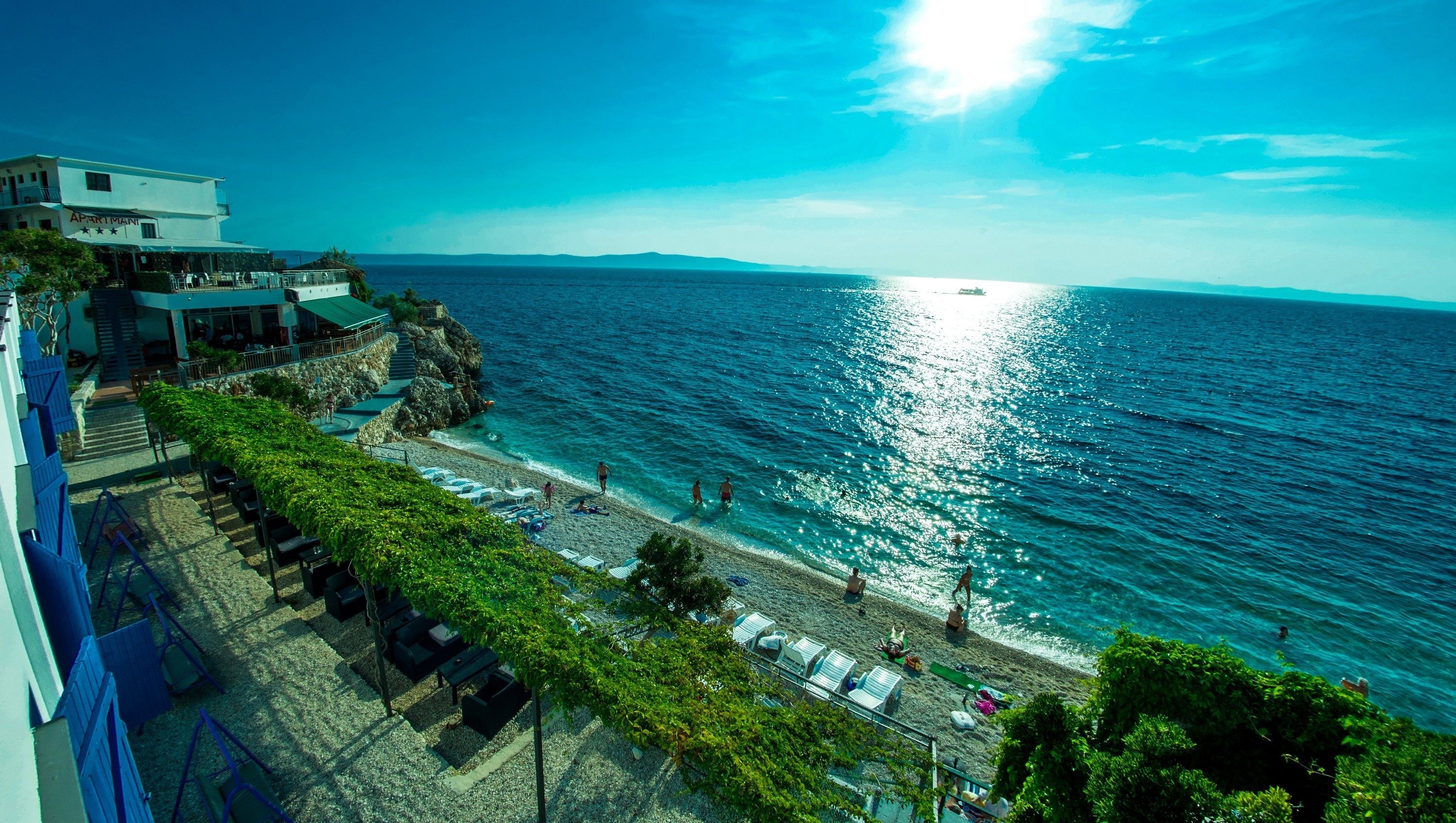 A coastal hotel with a beach view, outdoor seating, and a staircase leading to the upper levels.