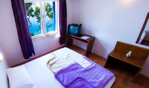 Una habitación de hotel con cama, escritorio con televisor y ventana con cortinas.