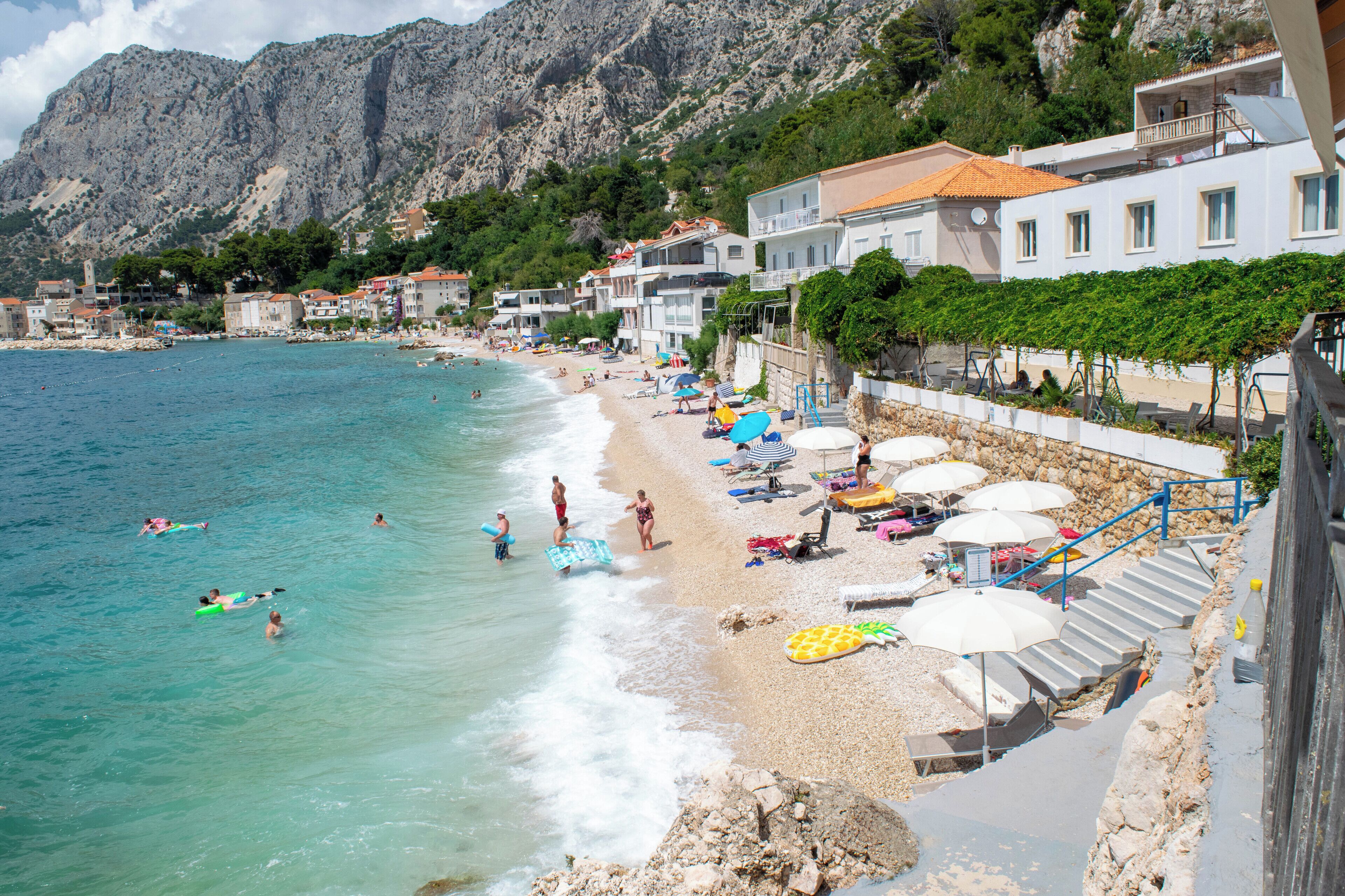 Una spiaggia costiera con acque limpide, un litorale roccioso e edifici con balconi affacciati sul mare.