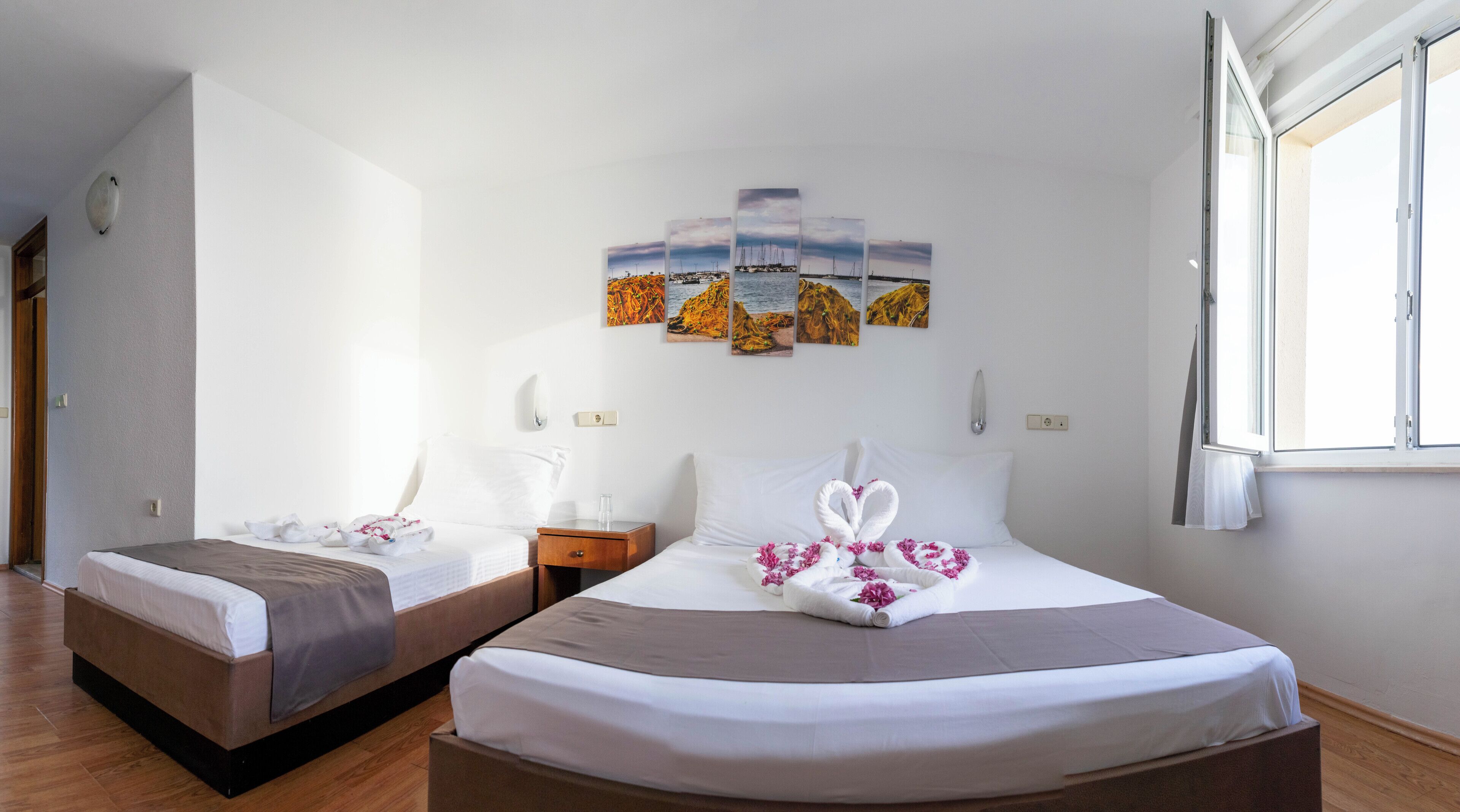 A hotel room with two beds, a wooden floor, a large window, and artwork on the wall.