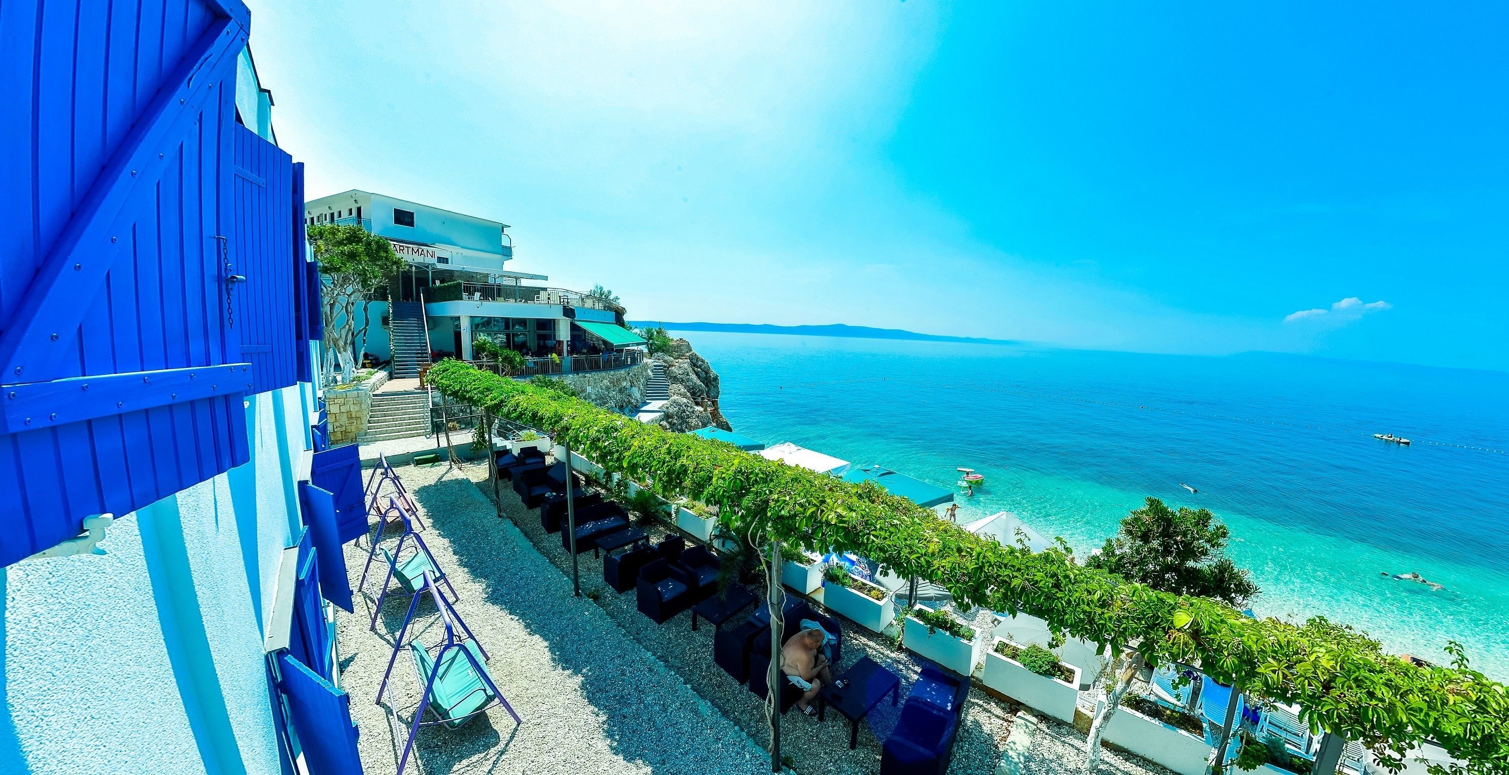 A seaside hotel with outdoor seating overlooking the ocean, a clear sky, and a view of the sea.