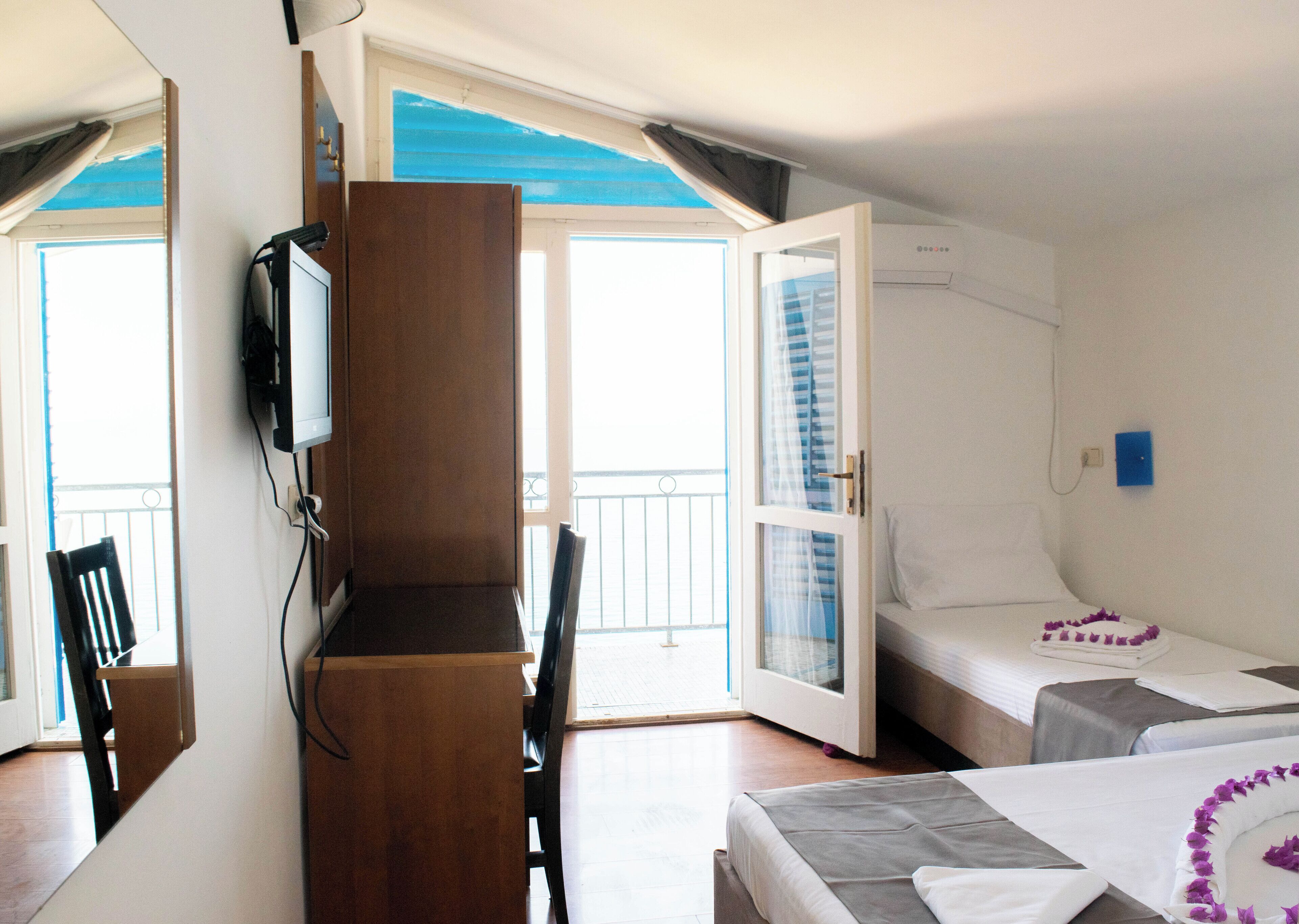 Una habitación con cama, escritorio y televisor. Incluye un balcón con barandilla y ventana.