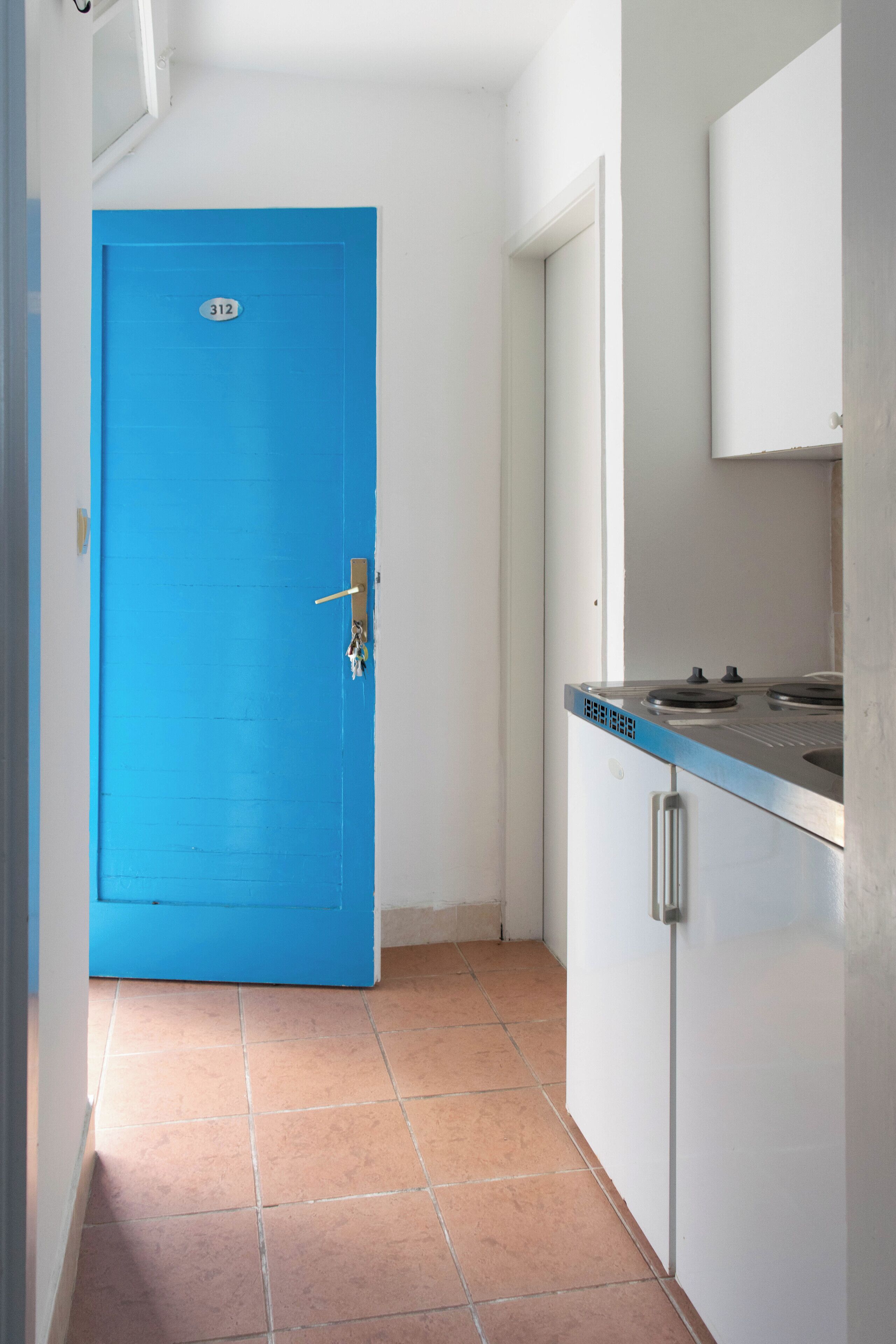 A narrow hallway with a blue door marked with the number 312, a stainless steel kitchen counter, and white cabinets.