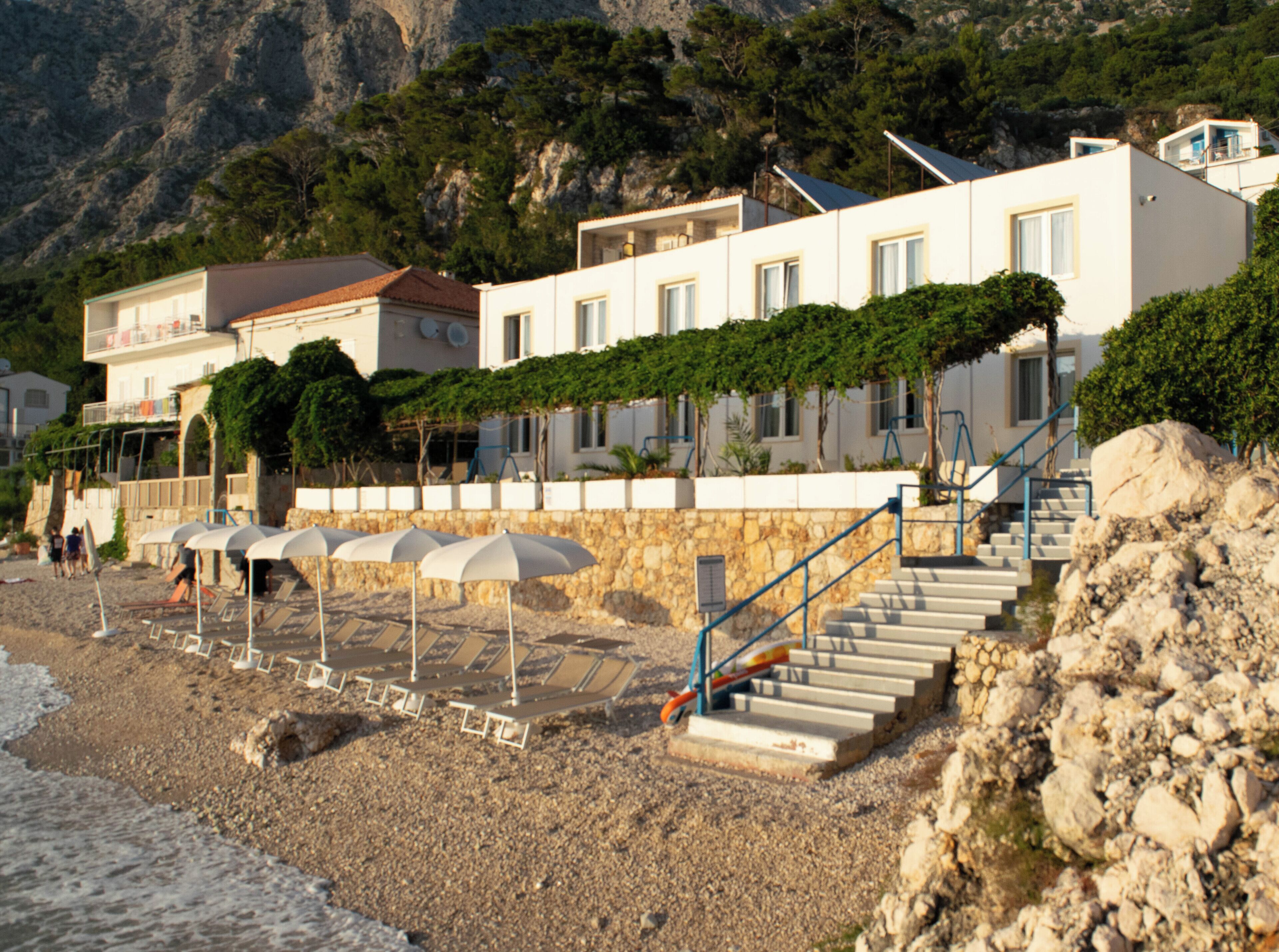 A coastal hotel with a stone facade, multiple balconies, and a staircase leading to the upper floors.