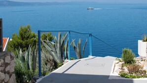 A coastal view with a clear sky, a boat on the water, and a concrete pathway leading to a gate. - Beach Hotel Plaza (Podgora)