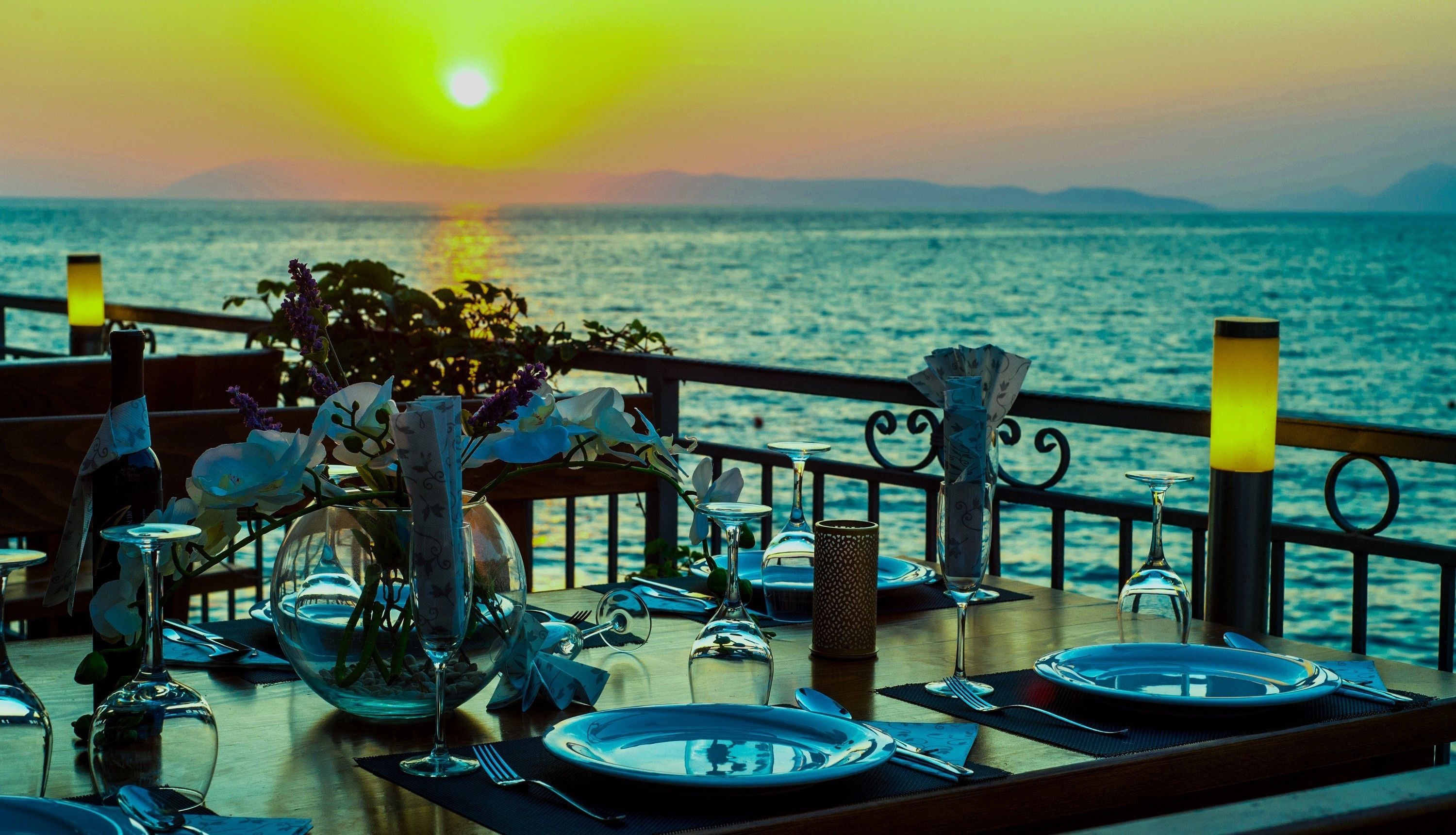 A table set for a meal with a view of the sea and a sunset in the background.
