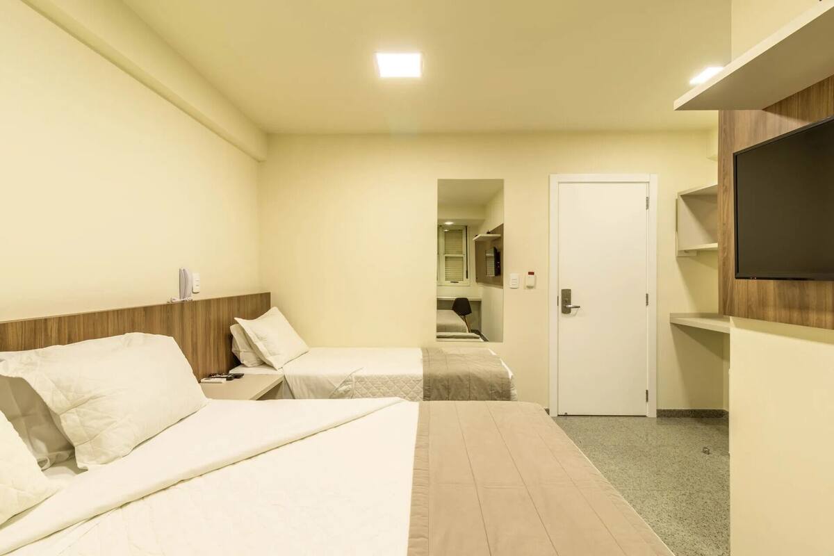 A hotel room with two beds, a TV mounted on the wall, and a door leading to a bathroom.