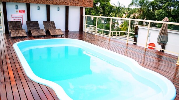 A swimming pool on a wooden deck with lounge chairs and a sign indicating maximum depth. - Hotel Dois H (Joinville)