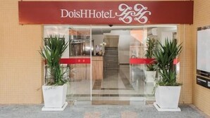 The exterior of DoisHotel with a red awning and two potted plants in front. - Hotel Dois H (Joinville)