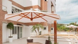 An outdoor patio with a table and chairs, a large umbrella, and a potted plant. - Hotel Dois H (Joinville)